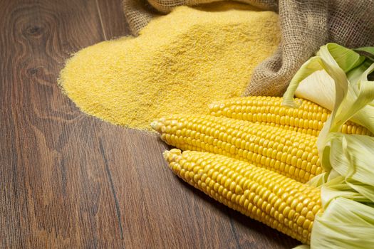 Ripe young sweet corn cob,on left stack cornmeal on wooden background, copy space.Gluten free food concept