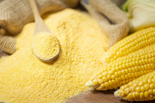 Ripe young sweet corn cob,on left stack cornmeal and spoon on top,wooden background, copy space.Gluten free food concept