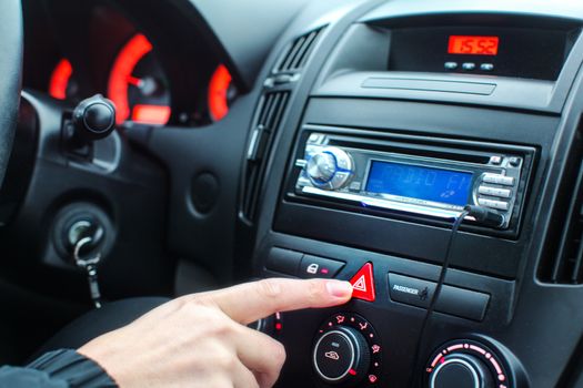 Detail on car dashboard, man finger pressing the emergency lights button while driving.