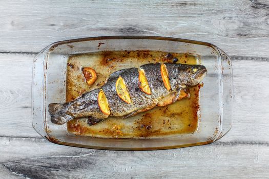 Table top view on grilled trout with lemons in glass baking pan, on gray wood desk.