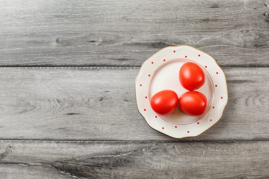 Table top view - three fresh tomatoes on white plate with small red dots and golden rim, laying on grey wood table.