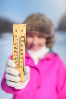 Young woman in pink sport jacket holding wooden thermometer outside on cold day, illustrating weather with temperature as low as -20 degrees Celsius.