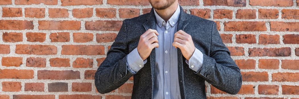 Suit man young businessman adjusting his blue coat smart casual outfit against brick wall background banner panorama at office. Urban lifestyle.