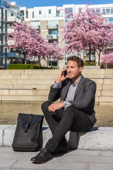 Man talking on smartphone. Businessman urban professional business man using mobile phone smiling drinking coffee at office building in city. Happy professional wearing suit jacket.