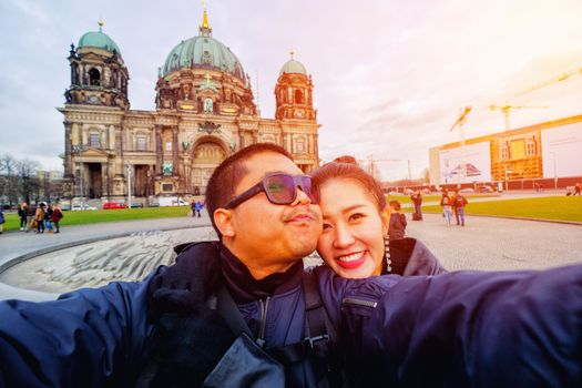 Young Couple Tourists selfie with mobile phone near Berlin Cathedral (Berliner Dom) at famous Museumsinsel (Museum Island) with Spree river in beautiful twilight time in summer, Berlin, Germany