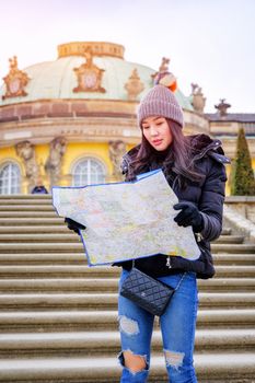 Young female tourist with map looking for a way to Sans Souci palace in Potsdam, Berlin, Germany, Europe.