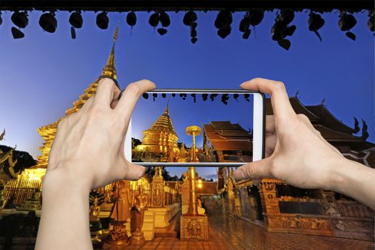 Woman Taking pictures on mobile smart phone showing Night view of Wat Phra That Doi Suthep, Chiang Mai, Popular historical temple in Thailand.