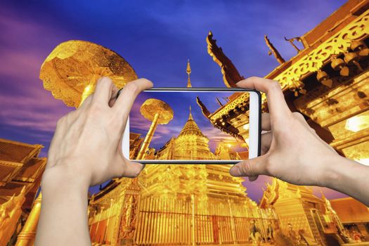 Woman Taking pictures on mobile smart phone showing Night view of Wat Phra That Doi Suthep, Chiang Mai, Popular historical temple in Thailand.