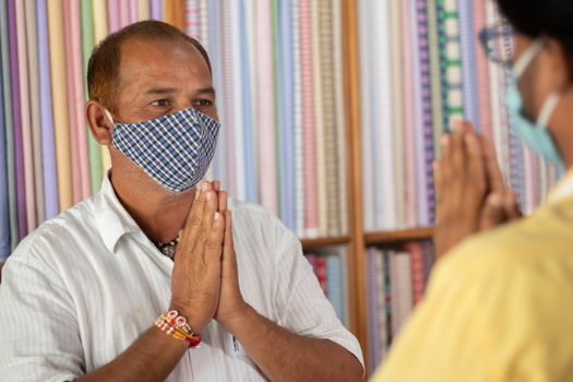 Shopkeeper greeting customer with namaste hand gesture and wearing medical mask to stop and spreading of coronavirus or covid-19 pandemic at workplace or shops - concept of new normal and business lifestyle