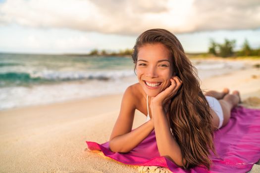 Happy Asian bikini wwoman model relaxing on summer vacation lying on beach towel, Hawaii travel.