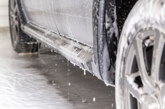 close-up view of silver car step at carwash with soap sud smudges and drops.