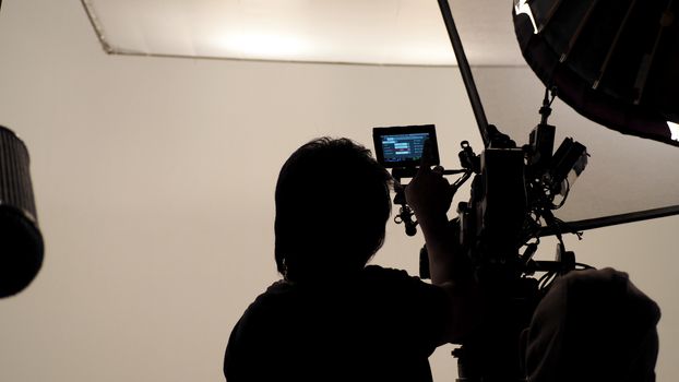 Silhouette of photographer checking for movie camera and set before shooting in studio.