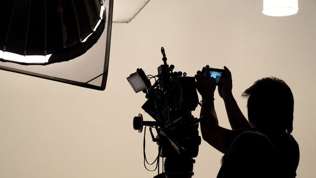 Silhouette of photographer checking for movie camera and set before shooting in studio.