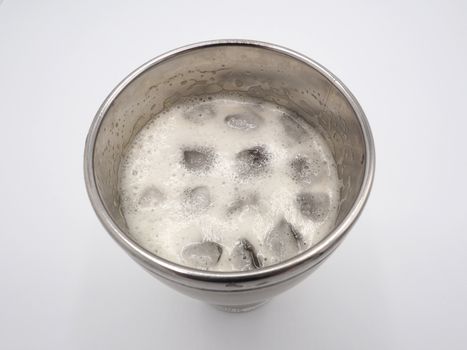 White beer foam bubbles and ice cubes close-up in the stainless steel thermos mug top view and white background.