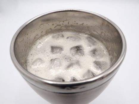 White beer foam bubbles and ice cubes close-up in the stainless steel thermos mug top view and white background.