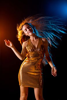 Portrait of dancing girl in golden dress on disco party blue and red studio lights