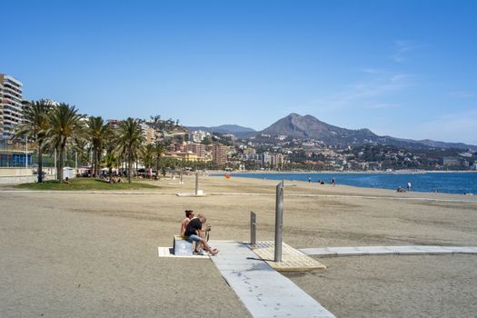 Malaga, Spain, April 2016: view on La Malagueta beach on a sunny and day with clear sky in summer. Palm trees, city architecture and mountains in the background