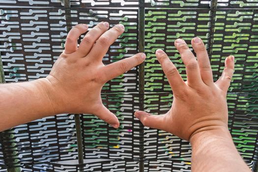 The hands of a locked man in a cage trying to escape through the bars