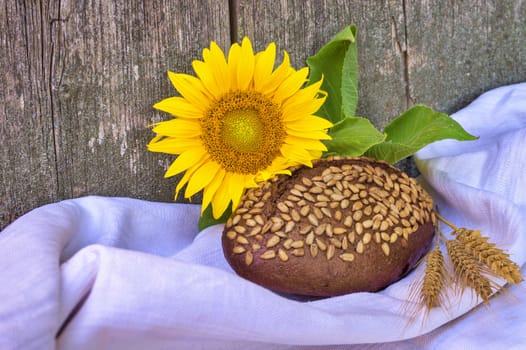 Healthy loaf of brown wholewheat bread coated in sunflower seeds with colorful fresh yellow sunflower and golden ears of wheat in a food still life