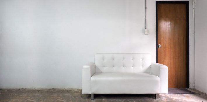 White leather sofa and white old wall and old wood door in room.