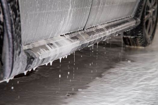 close-up view of silver car step at carwash with soap sud smudges and drops.