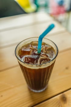 Cup of iced coffee with straw on wooden table