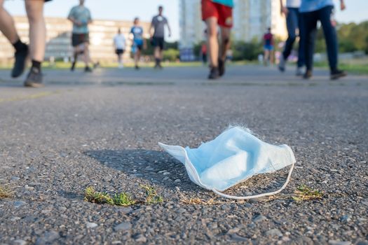 a dangerous discarded anti-virus breathing mask lies on the road against the background of passing people