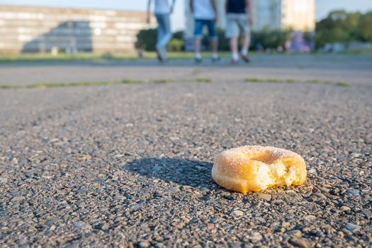 a discarded delicious sweet nibbled doughnut, a bun, lies on the pedestrian path of the stadium, where people pass by