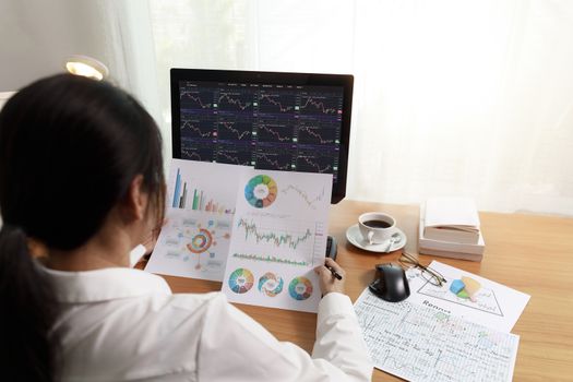Rear view business woman working in office with computer holding chart report paper and looking. business people analysis stock market, forex chart data on PC screen and paper. Business and finance concept.