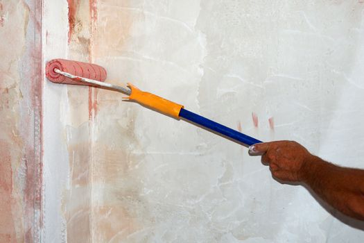 male hand with paint roller applies primer to the wall close up