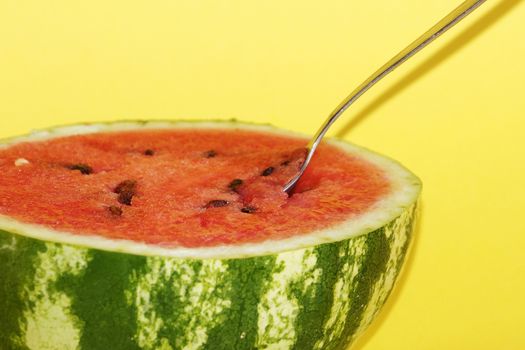 half watermelon with a spoon on a yellow background close up