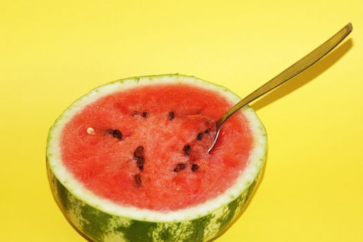 half watermelon with a spoon on a yellow background close up