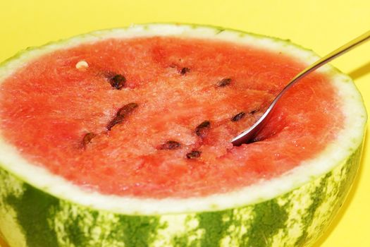 half watermelon with a spoon on a yellow background close up