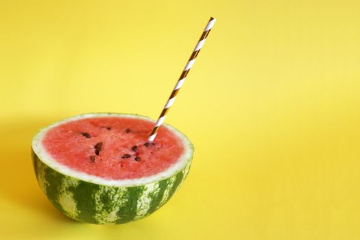 half watermelon with cocktail straw on yellow background, close up