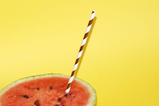 half watermelon with cocktail straw on yellow background, close up