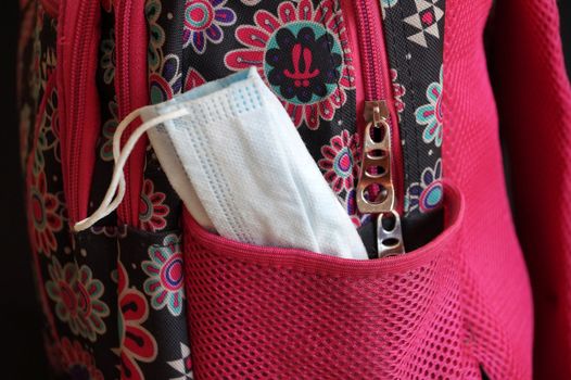 a medical mask sticking out of a school backpack close up