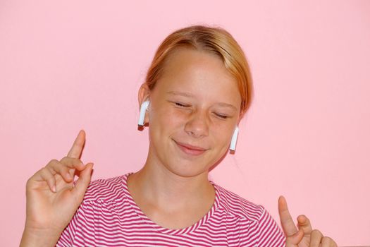 teenage girl listening to music with closed eyes on headphones and smiling, portrait on pink background