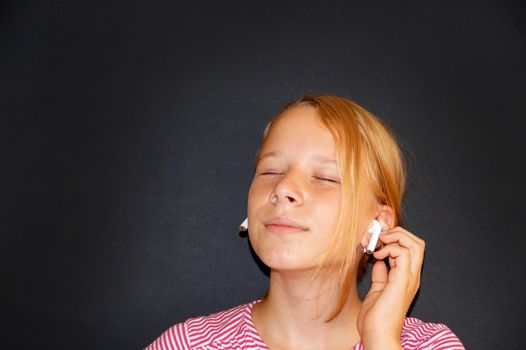 teenage girl listening to music with closed eyes on headphones and smiling, portrait on black background