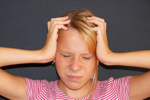 teenage girl with closed eyes holds her sore head with her hands.