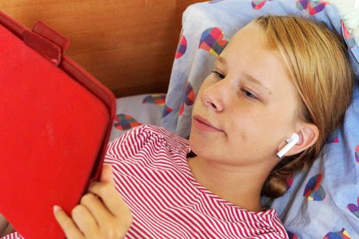 teenage girl in headphones looking tablet while lying in bed.
