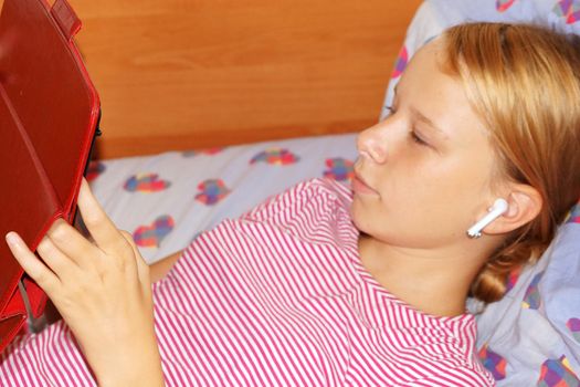 teenage girl in headphones looking tablet while lying in bed.