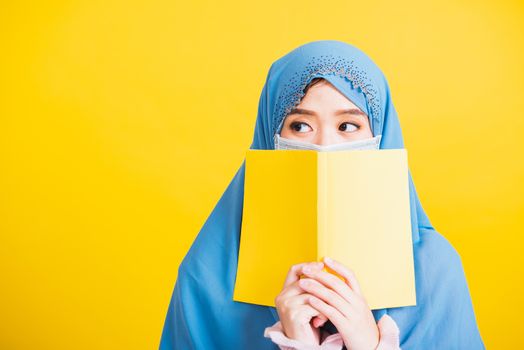 Asian Muslim Arab, Happy beautiful young woman religious wear veil hijab and face mask to prevent coronavirus she student hold books close face, isolated on yellow background, Back to college