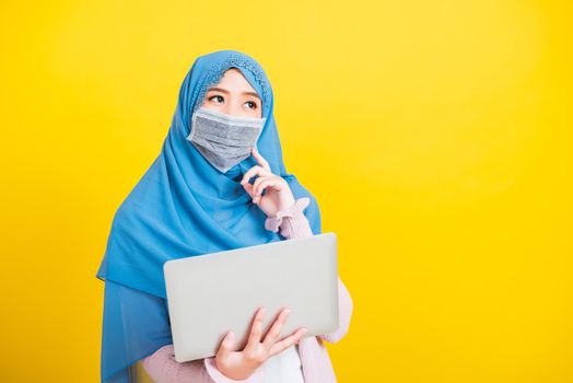 Asian Muslim Arab, Portrait of happy beautiful young woman Islam religious wear veil hijab and face mask protect she quarantines disease coronavirus hold laptop computer and thinking question