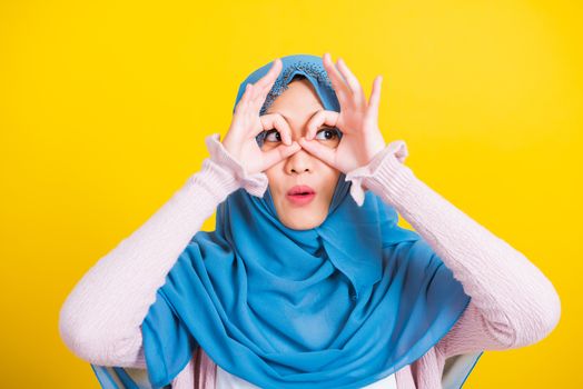 Asian Muslim Arab, Portrait of happy beautiful young woman Islam religious wear veil hijab funny smile she show gesture fingers in okay gesture symbol, OK sign over her eyes isolated yellow background