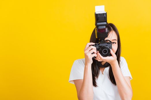 Portrait of happy Asian beautiful young woman photographer smile take picture and looking viewfinder on retro digital mirrorless photo camera ready to shoot, studio shot isolated on yellow background