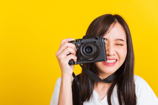 Portrait of happy Asian beautiful young woman photographer smile take picture and looking viewfinder on retro digital mirrorless photo camera ready to shoot, studio shot isolated on yellow background
