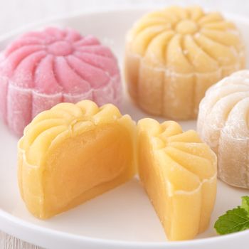 Colorful snow skin moon cake, sweet snowy mooncake, traditional savory dessert for Mid-Autumn Festival on bright wooden background, close up, lifestyle.