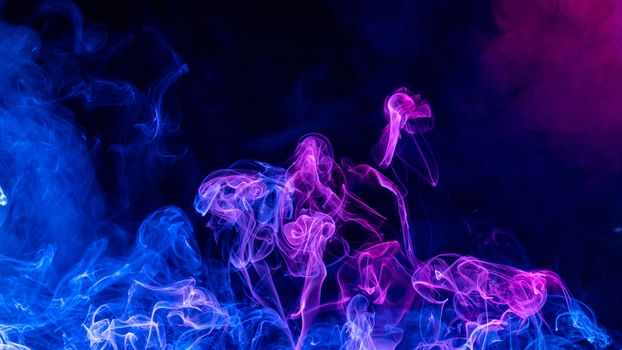 Conceptual image of multi-colored smoke isolated on dark black background, Halloween design element.