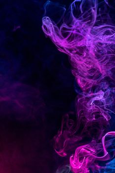 Conceptual image of multi-colored smoke isolated on dark black background, Halloween design element.