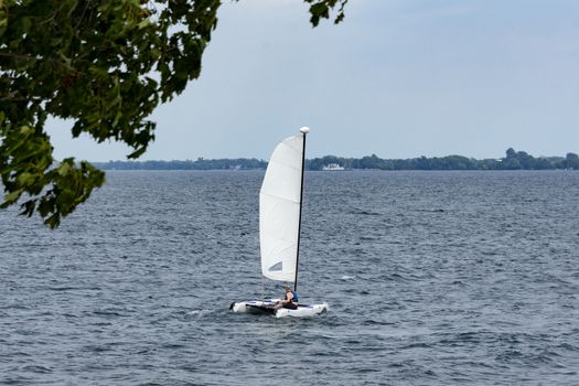 A man is sailing on a catamaran to the opposite shore of the lake